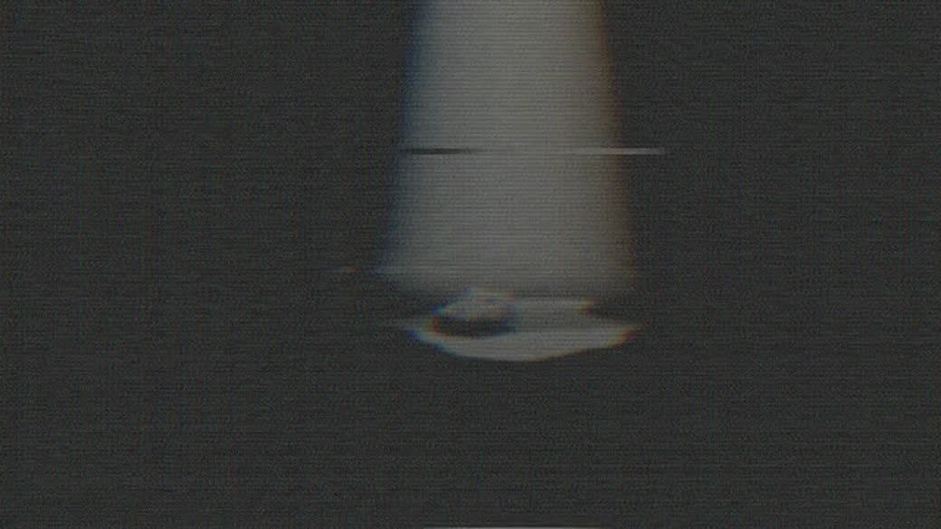 A dim cave passage rendered with glitch texture, light breaking apart around a distant pale source at the end of the walk.
